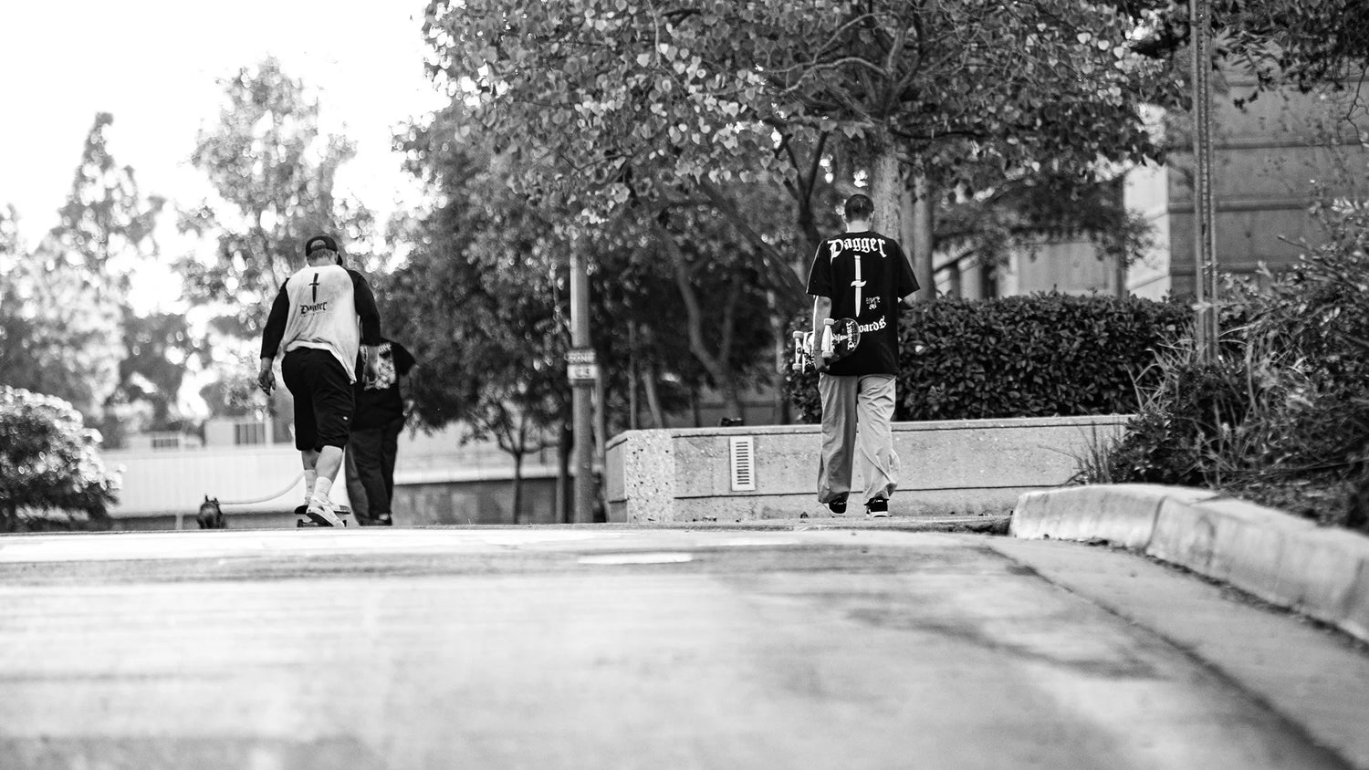 Skater walking with skateboard wearing Dagger shirt — black and white street photo